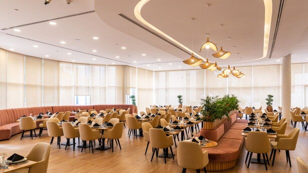 A spacious dining area with round tables and chairs, a curved ceiling with recessed lighting, and large windows allowing natural light. - eStay Hotel  (Dubai)