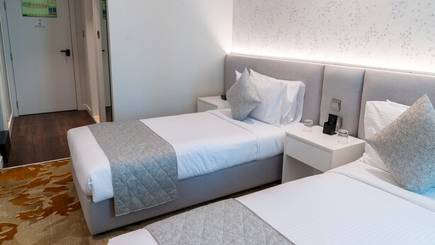 A hotel room with two beds, a bedside table with a lamp, and a carpeted floor. - eStay Hotel  (Dubai)