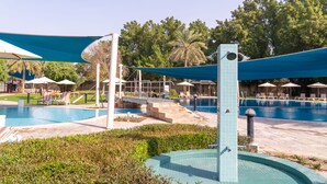 A swimming pool area with lounge chairs and umbrellas, surrounded by greenery and palm trees. - eStay Hotel  (Dubai)