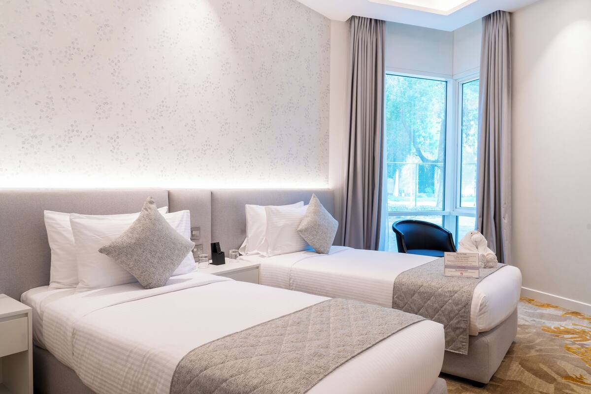 A hotel room with two beds, a large window with curtains, and a view of the outdoors.
