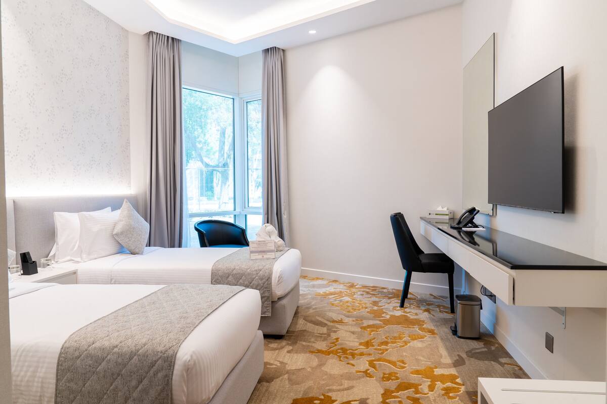 A hotel room with two beds, a desk, a chair, a TV, and a window with curtains.