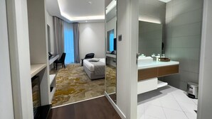A modern hotel room with a bed, a desk, a chair, a large mirror, and a bathroom with a sink and toilet. - eStay Hotel  (Dubai)