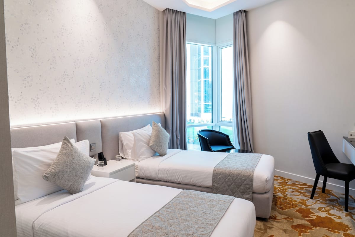 A hotel room with two beds, a desk, a chair, and a view of the outdoors.