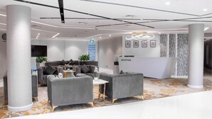 A modern reception area with a reception desk, grey sofas, and a patterned carpet. - eStay Hotel  (Dubai)