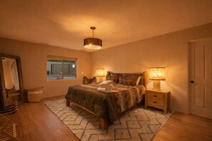 A bedroom with a bed, bedside lamps, a wooden floor, a window, and a door.