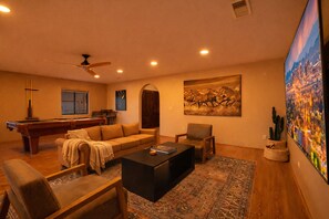 A living room with a pool table, a sofa, a coffee table, and a large painting.