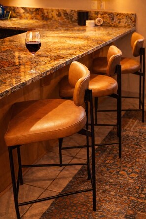 A bar area with a granite countertop, leather bar stools, and a glass of red wine.