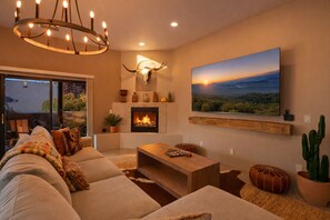 A cozy living room with a fireplace, a large landscape painting, and a modern chandelier.