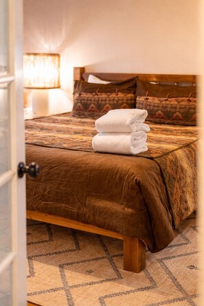 A neatly made bed with a brown bedspread and a stack of white towels. - Red Rock Views • Pool, Spa, Firepit, & Billiards • Luxe 6BR Sedona Retreat (Sedona)