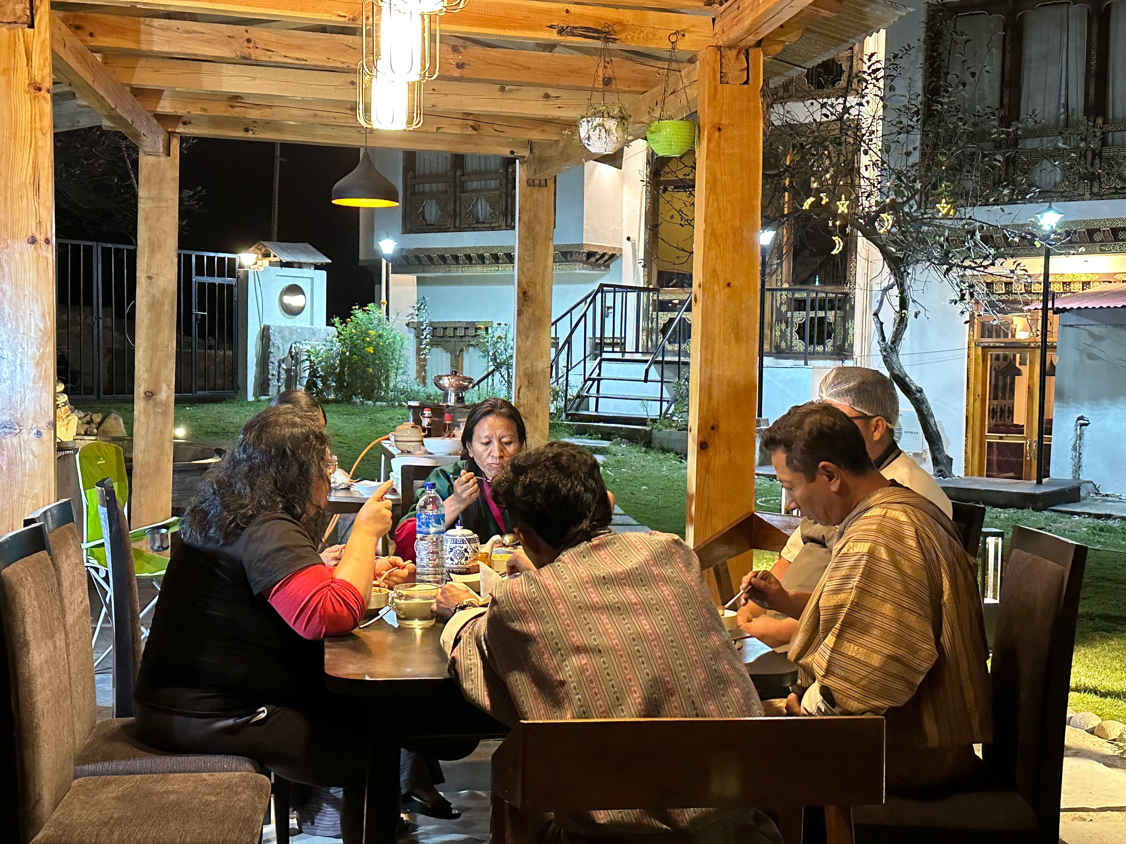 Un espace de restauration en plein air, avec des tables et des chaises en bois, entouré d’un jardin et d’un bâtiment à l’architecture traditionnelle.