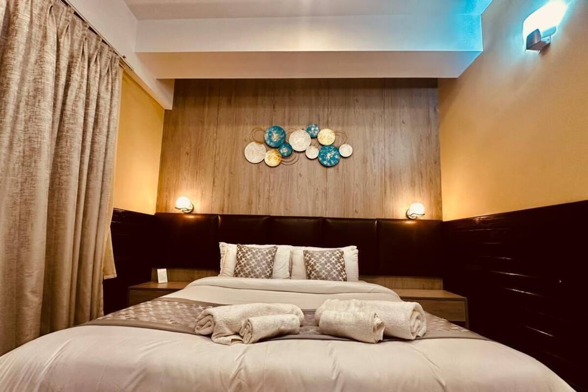 A neatly made bed with a headboard, a wall-mounted light fixture, and a decorative wall piece.