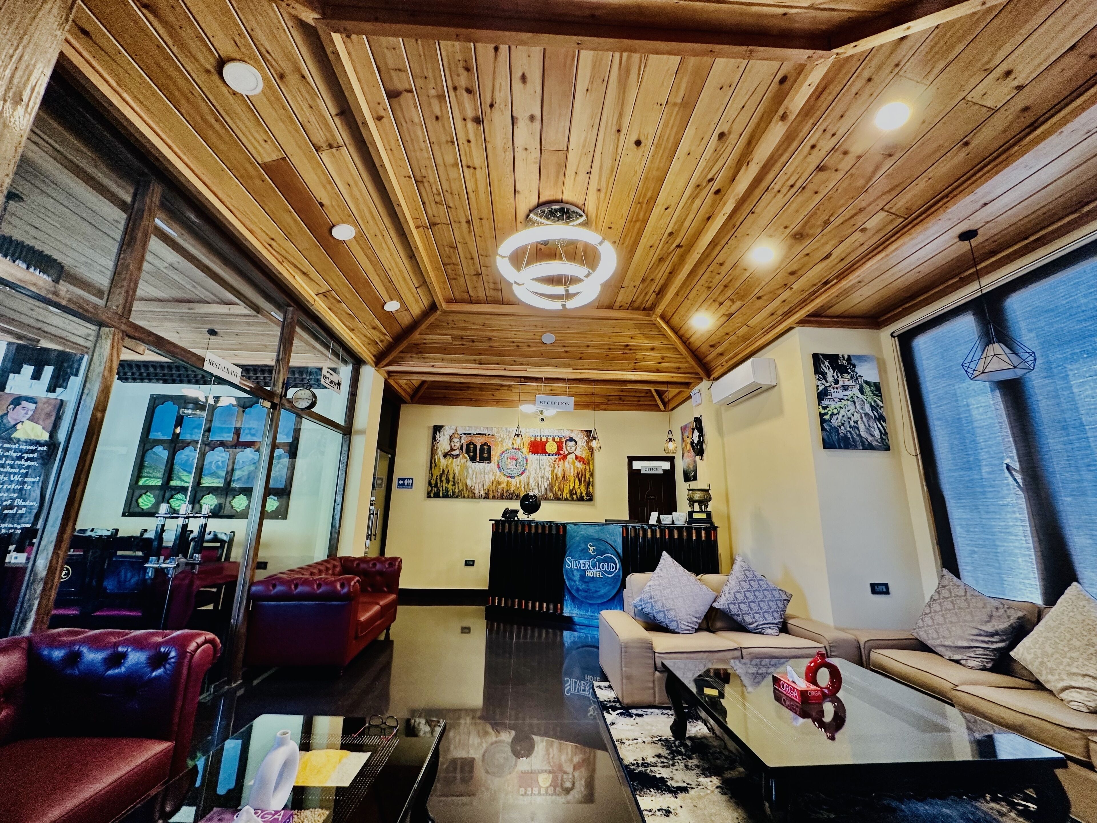 Eine geräumige Hotelhalle mit Holzbalkendecke, einer Rezeption, Ledersofas und einem großen Fenster mit Blick auf die Berge.