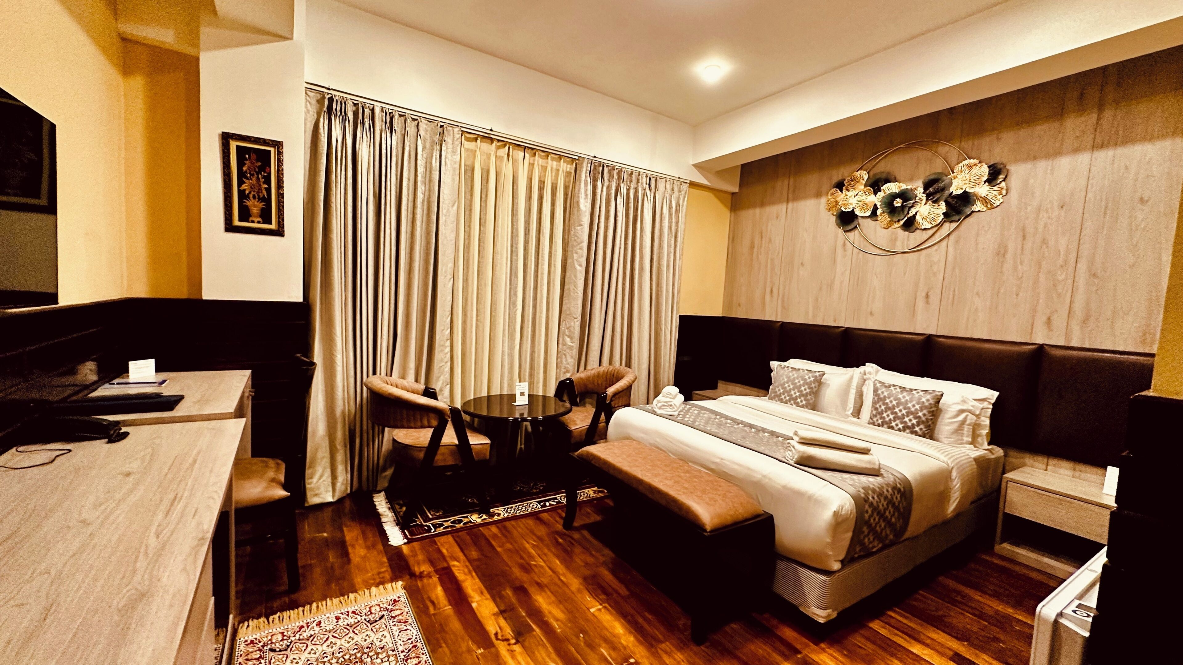 Une chambre d’hôtel avec un lit, un bureau, une chaise, une petite table et un rideau.