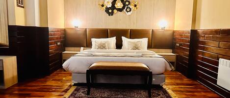 Un dormitorio con piso de madera, una cama con ropa blanca, dos lámparas de noche y un adorno en la pared sobre la cama.