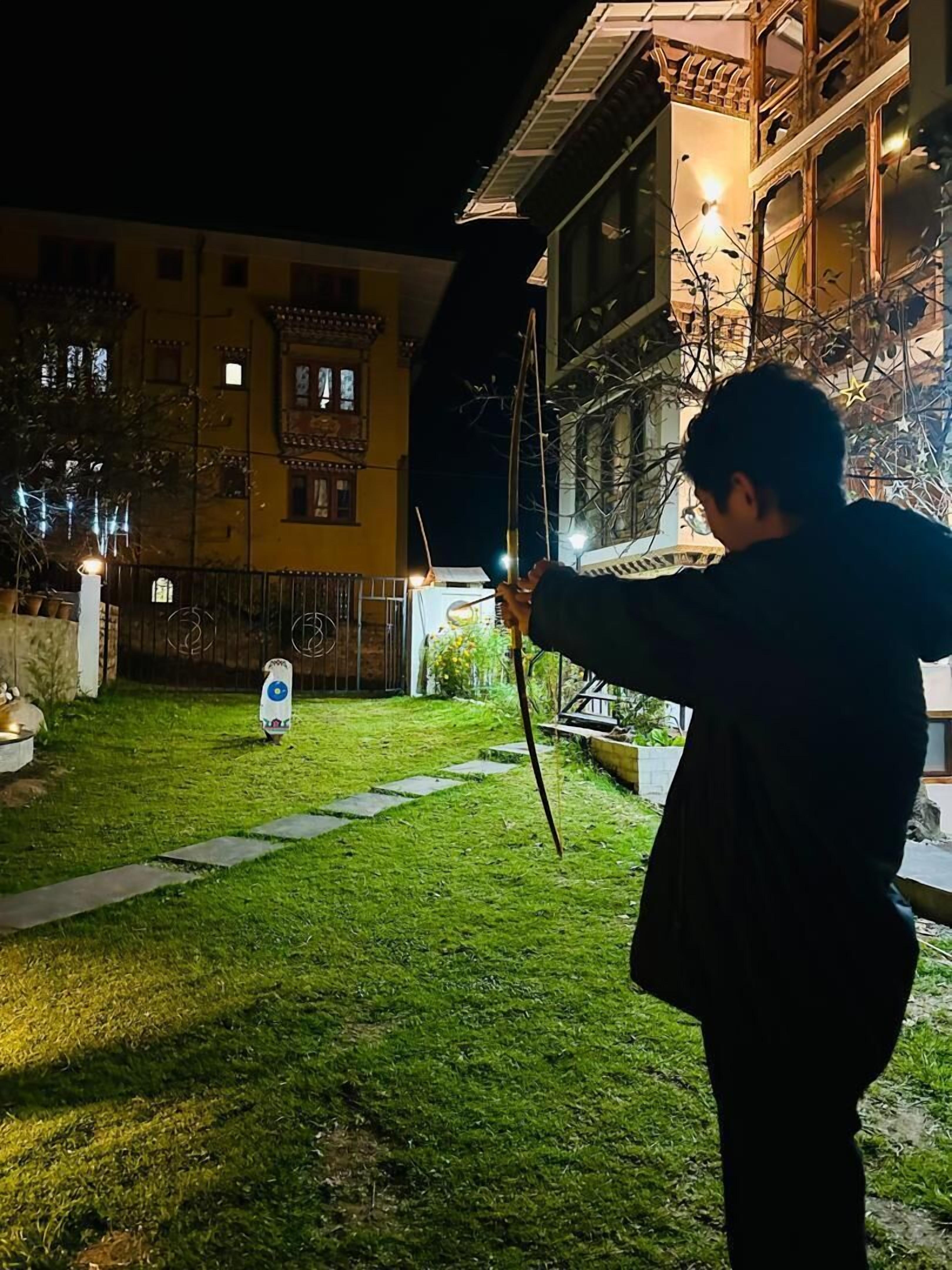 Una persona sosteniendo un paraguas negro en un patio luminoso, con un sendero que lleva a un edificio con múltiples ventanas y balcones.