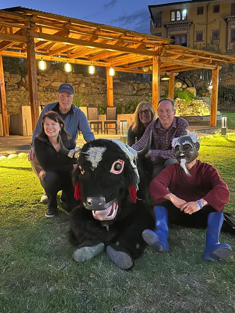 A group of people posing with a large, black and white cow statue in a covered outdoor area with stone walls and a wooden pergola.