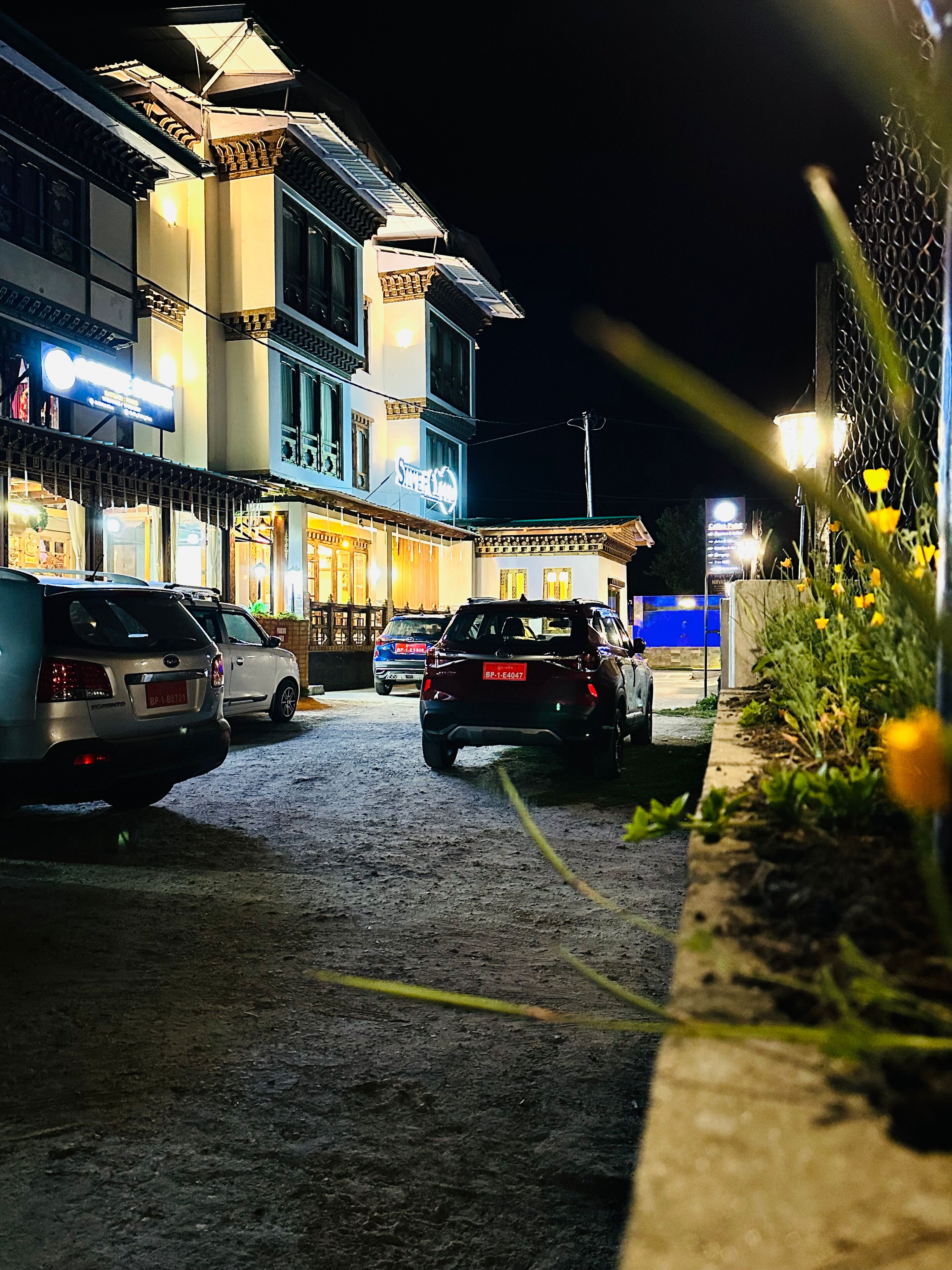 Una calle iluminada de noche, con coches aparcados y edificios iluminados.