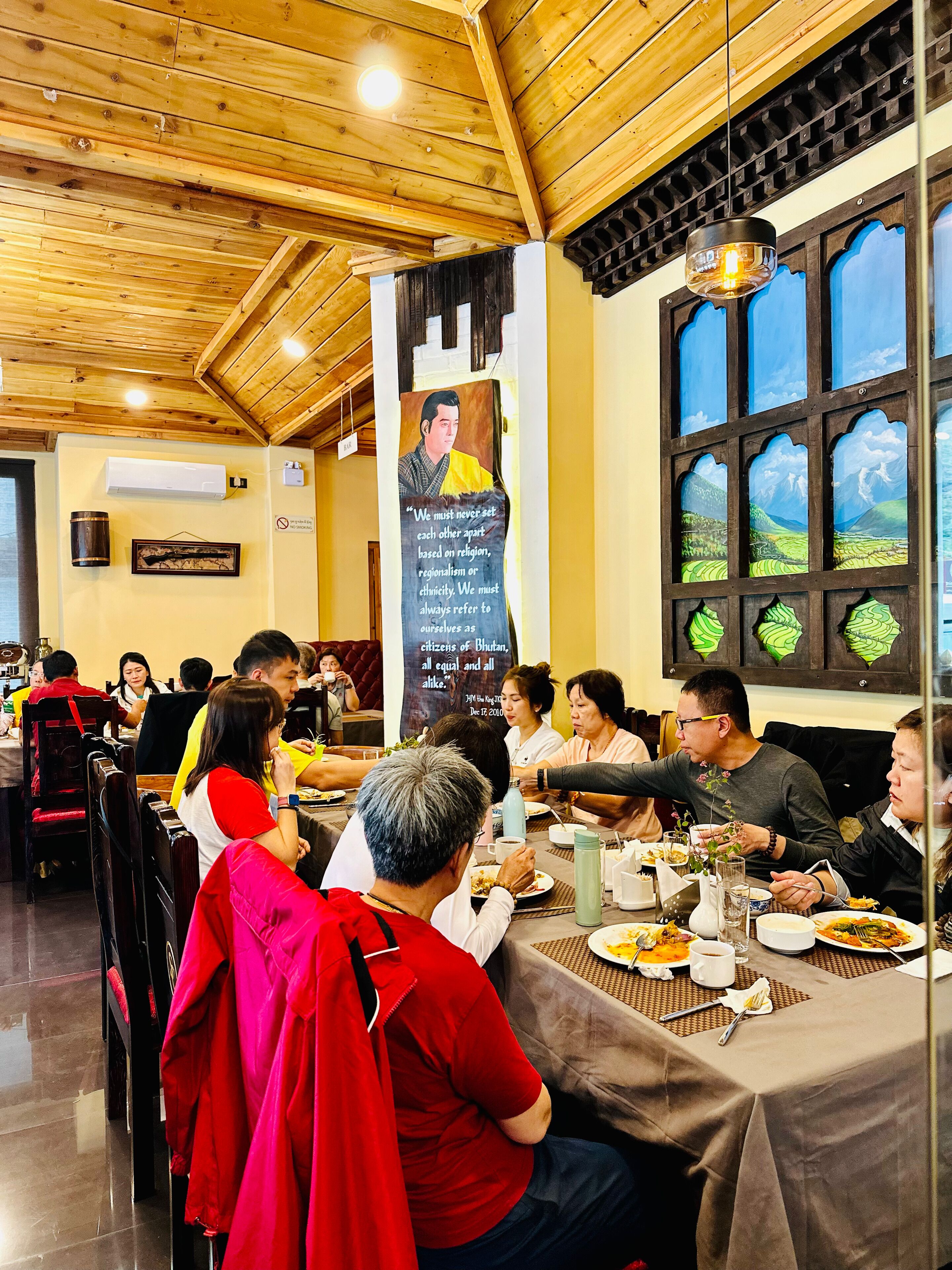 A restaurant with wooden ceiling beams, a banner with a quote, and a view of green fields through the windows.