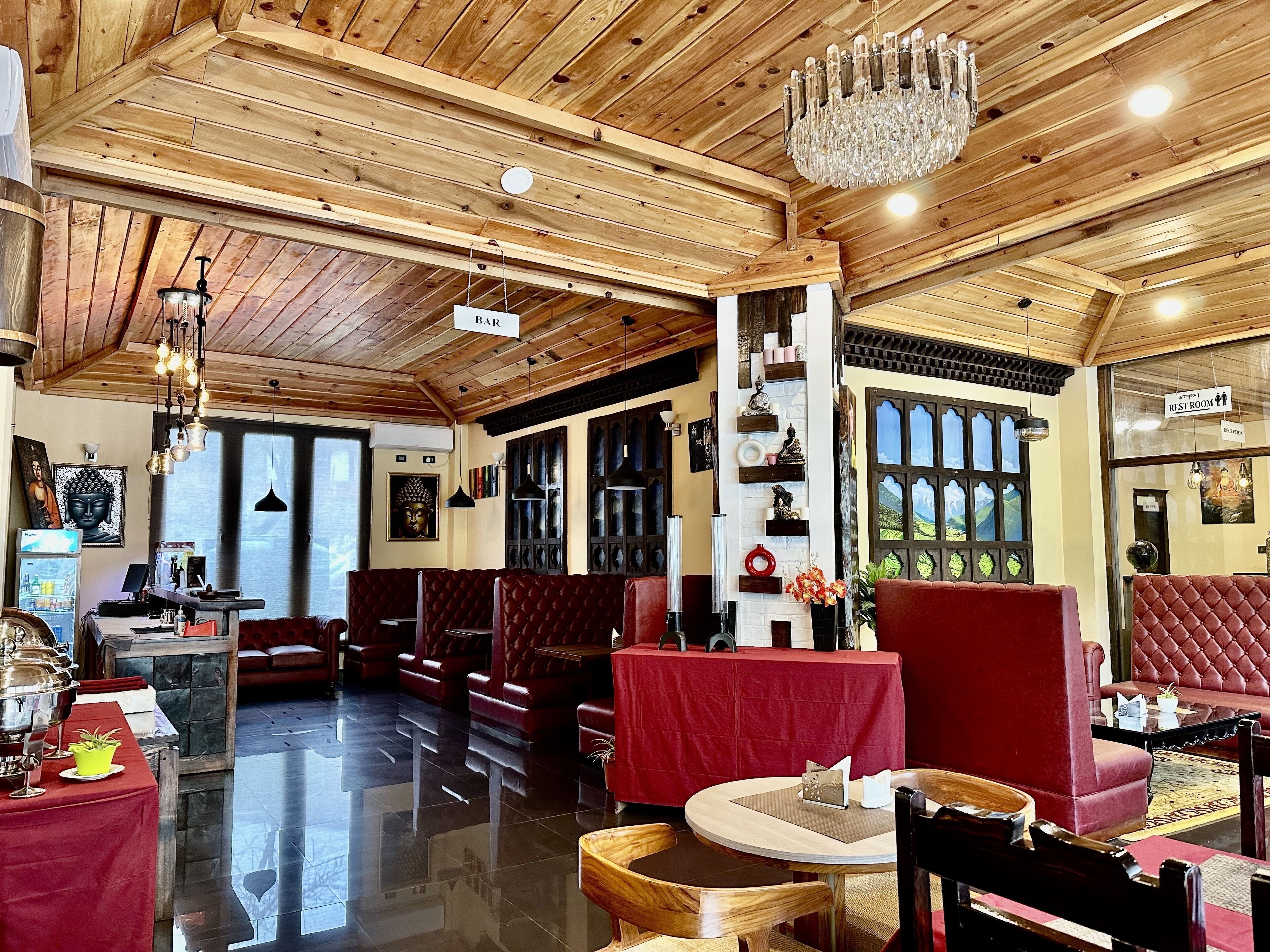 A spacious lobby with wooden ceiling beams, a chandelier, and red cushioned seating areas.