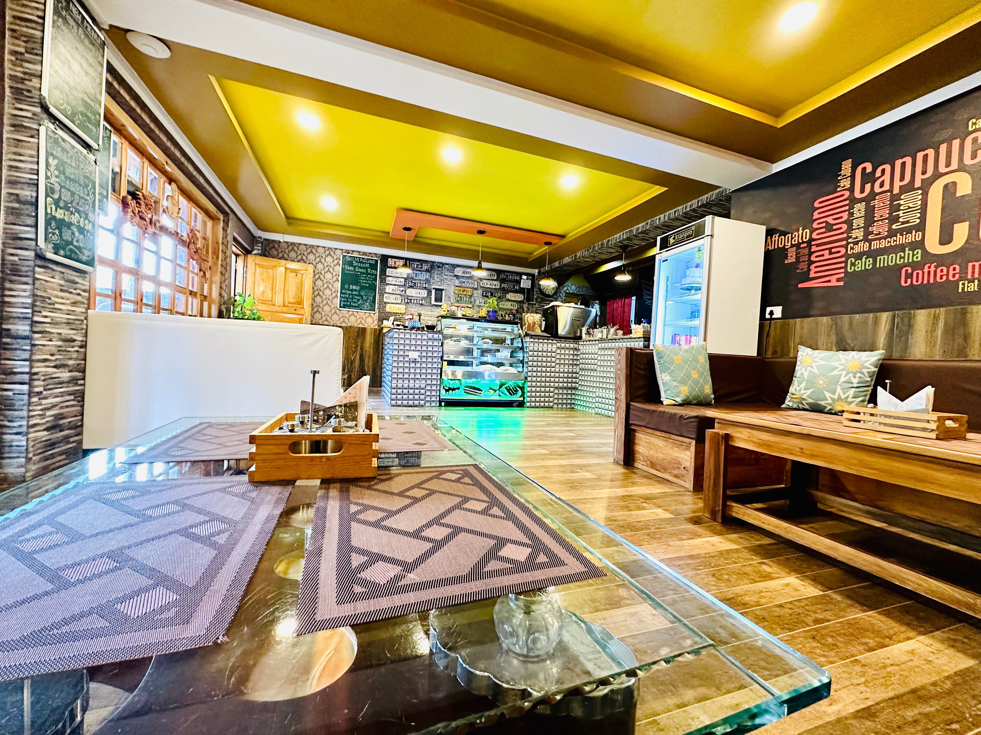 A modern cafe interior with a glass table, wooden seating, and a menu board on the wall.