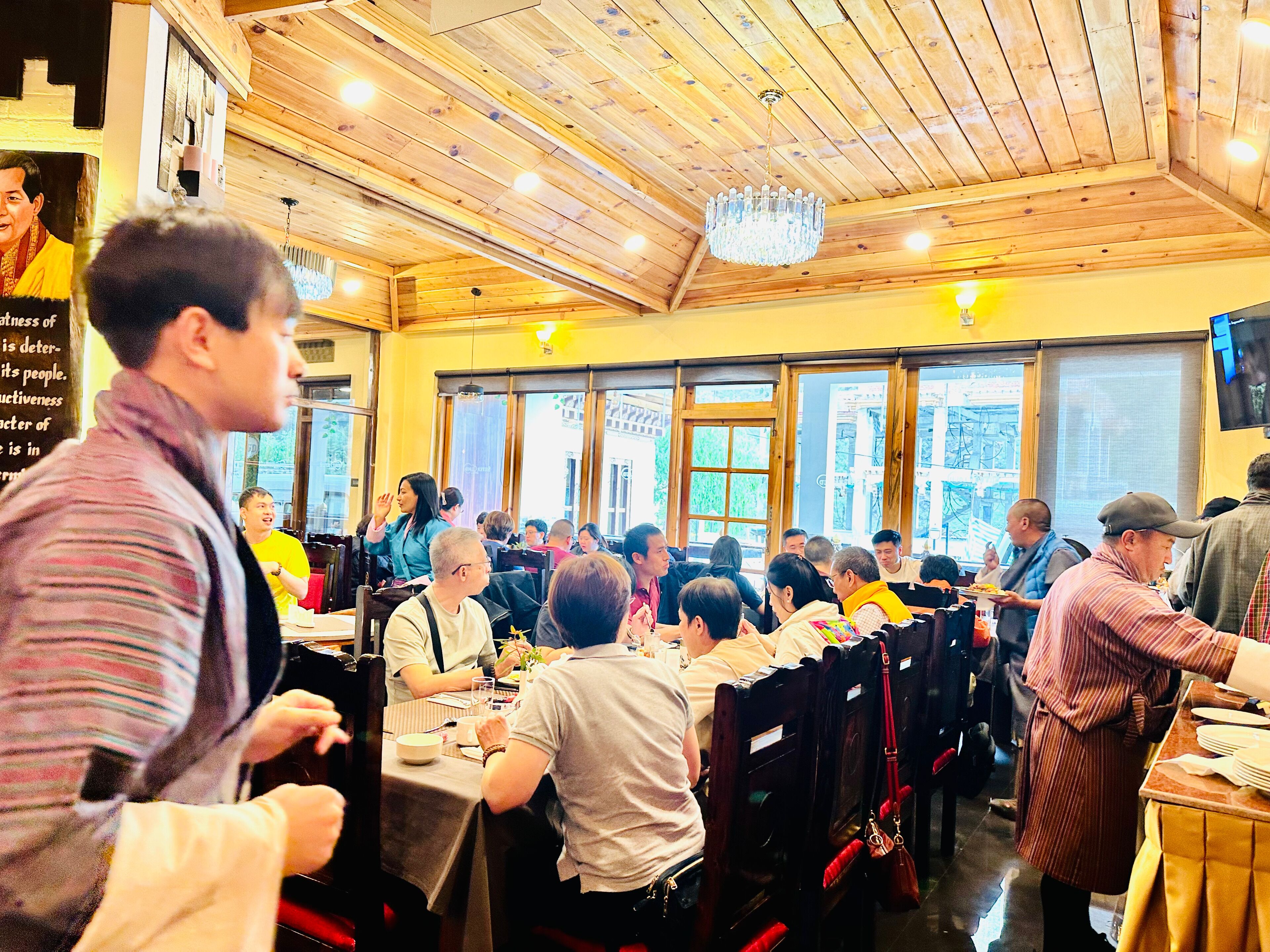 A restaurant with wooden ceiling and walls, large windows, and a chandelier.
