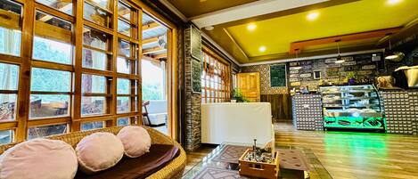 A cozy room with a large window, a wicker sofa with cushions, a glass coffee table, and a reception area with a counter and display cases.