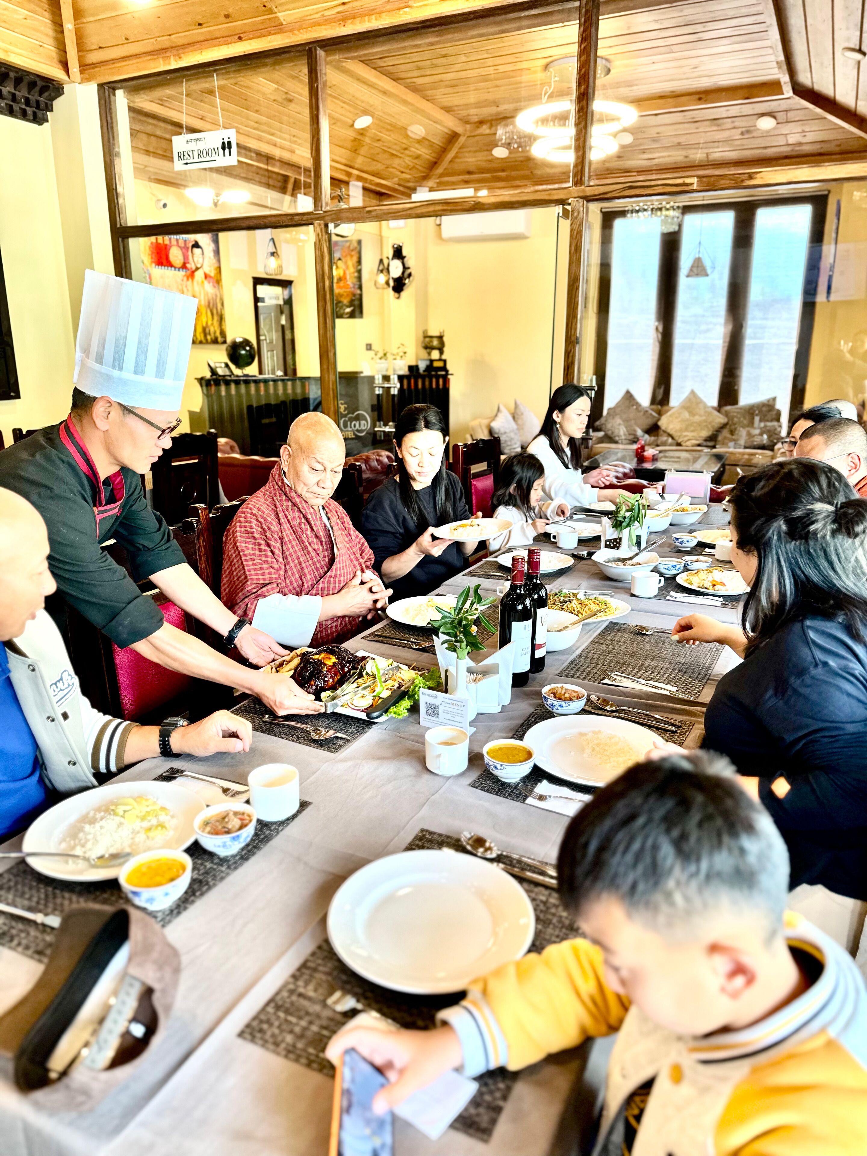 Un groupe de personnes est réuni dans un restaurant, qui se distingue par son plafond en bois et ses grandes fenêtres.