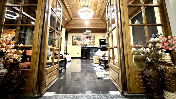 Un hall d’hôtel avec des portes en bois, un lustre, un comptoir d’accueil et un grand miroir.