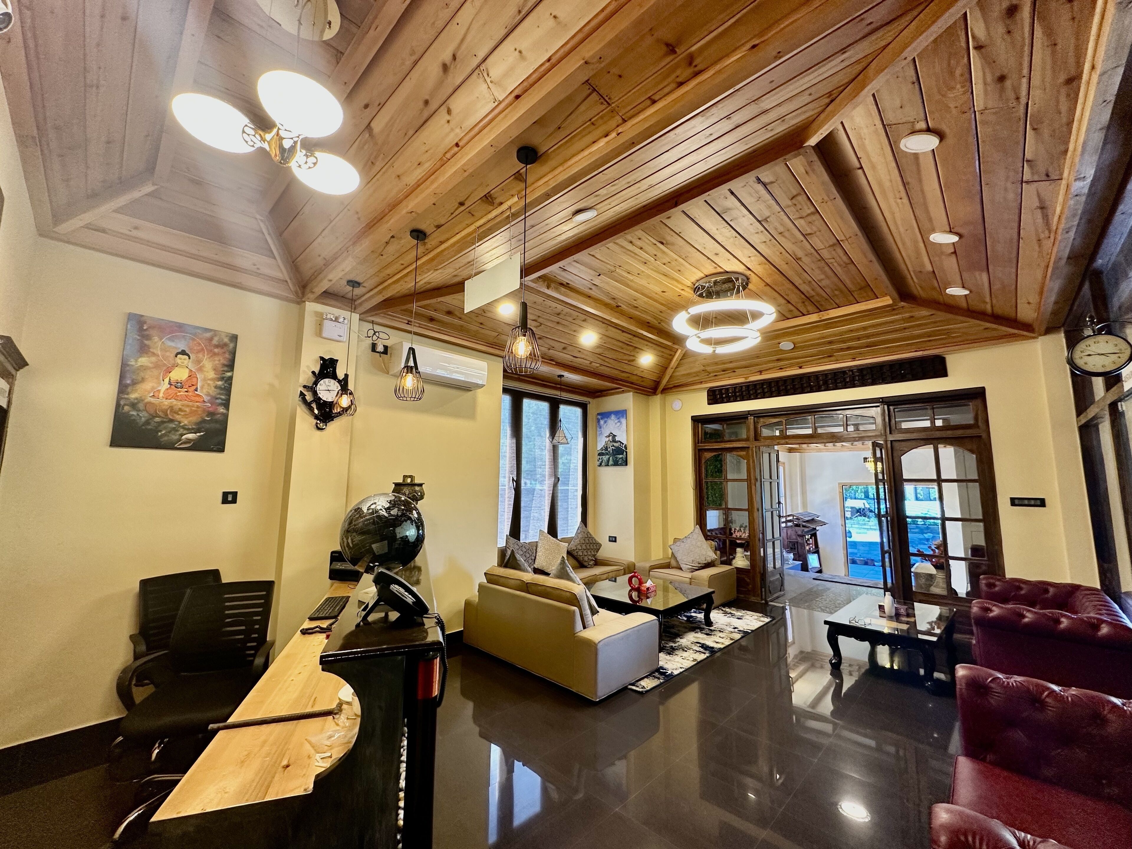 A spacious lobby with wooden ceiling beams, a reception desk, seating area, and a view through the glass doors.