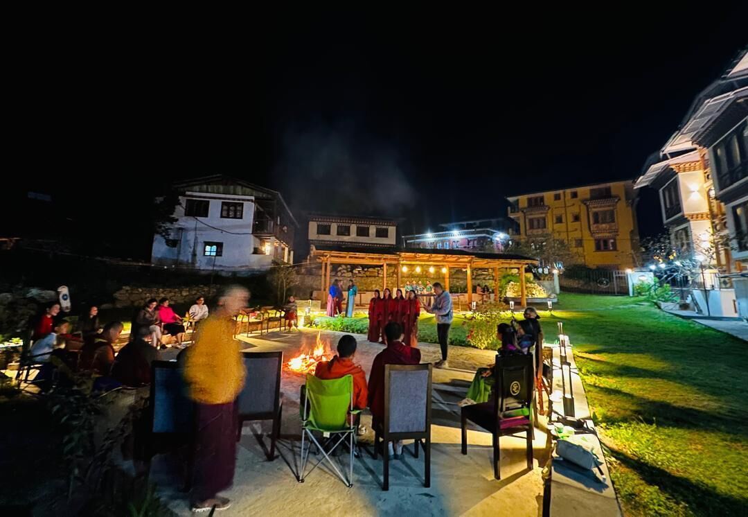 An outdoor dining area with tables and chairs, a fire pit, and a group of people gathered around.