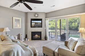 A living room with a fireplace, a ceiling fan, a TV, and a balcony with outdoor furniture. - Cedar Heights Delight-Waterfront, Pools, Wet Bar, & More! (Camdenton)