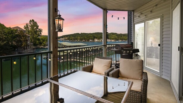 Un balcon agrémenté de meubles en osier, d’une table et offrant une vue sur un plan d’eau et des collines.
