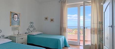 A bedroom with two beds, a nightstand, a dresser, and a balcony with a view.