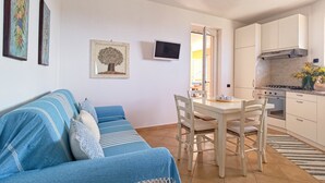 A modern kitchen with white cabinets, a dining table, and chairs. There is a blue sofa with striped cushions and a decorative tree painting on the wall. - Elegant apartment with sea view (Nebida)