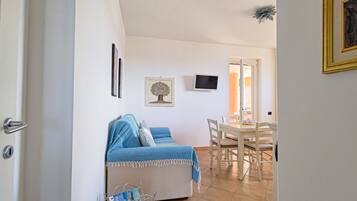 Een woonkamer met een bank, een eettafel met stoelen, een televisie en een ingelijst schilderij aan de muur.