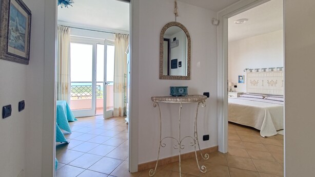 A hotel room with a balcony, a bed, a small table with a mirror, and a wall-mounted light fixture. - Elegant apartment with sea view (Nebida)