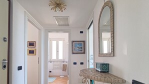 A hallway with a tiled floor, a round table with a decorative top, a mirror with a brick frame, and a door leading to another room. - Elegant apartment with sea view (Nebida)