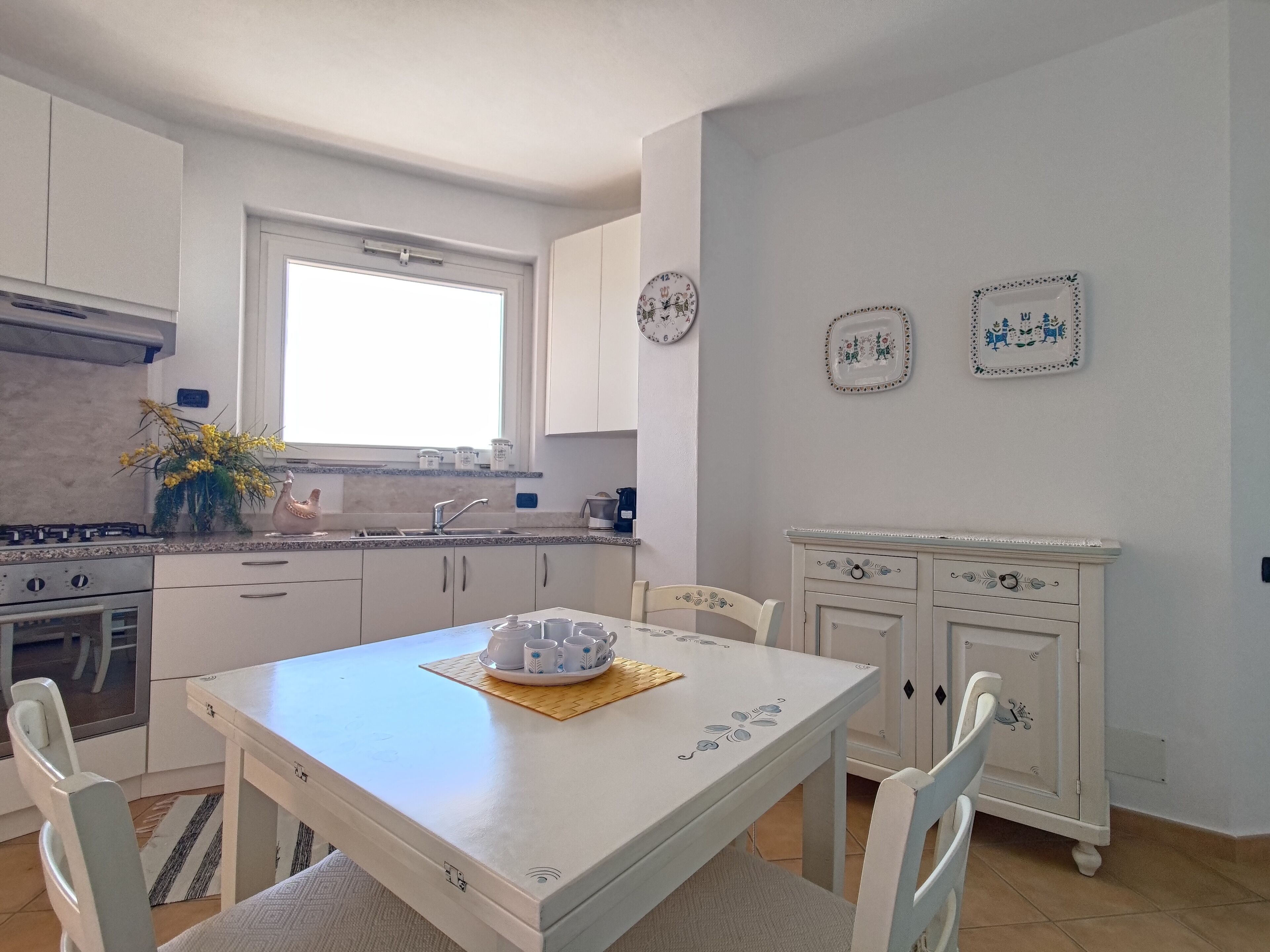 A kitchen with white cabinets, a window, a sink, and a dining table with chairs.