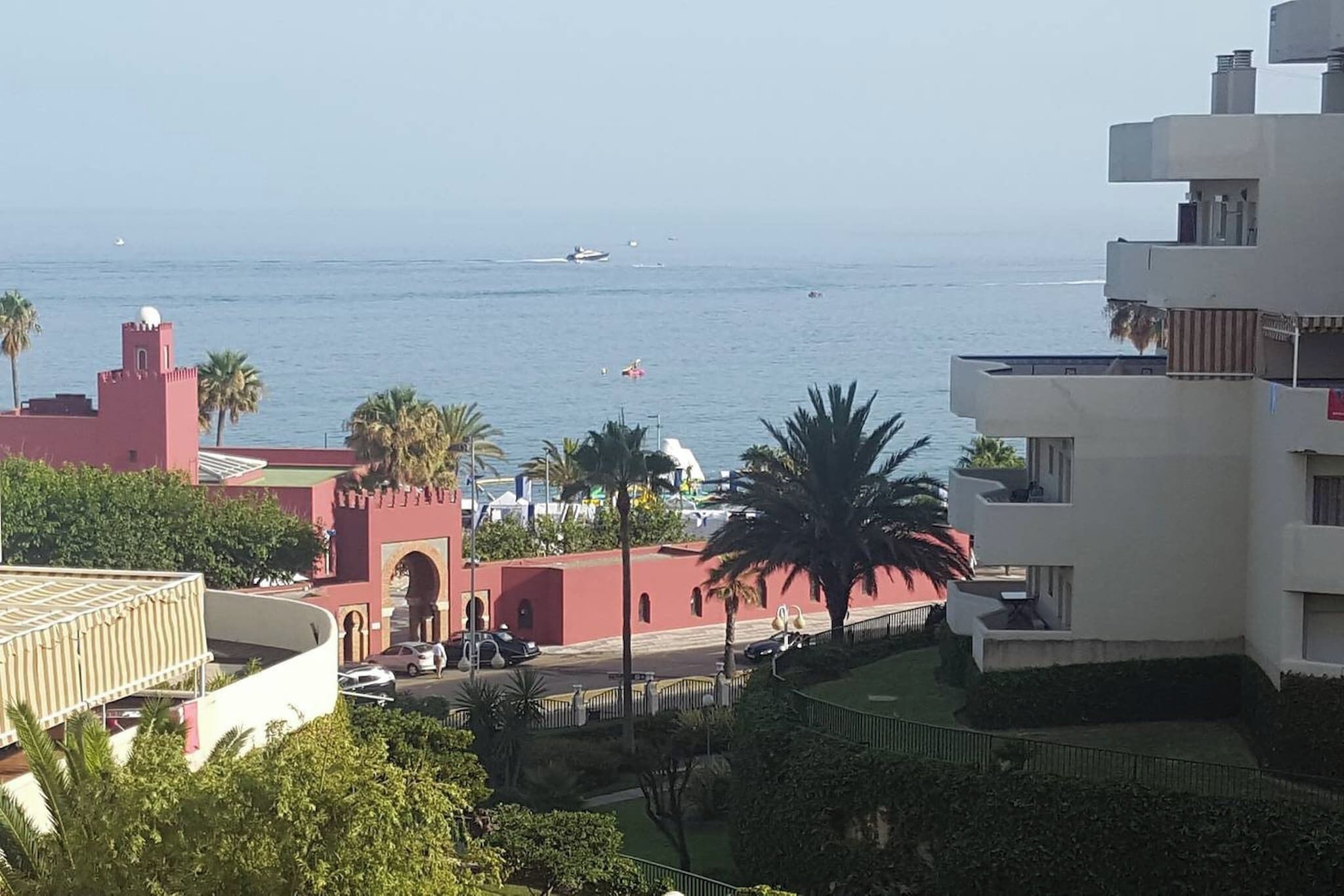 A coastal view with a building featuring a red tower and a white structure with balconies.