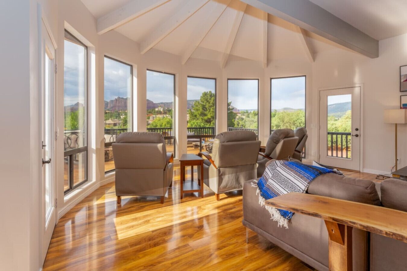 A spacious living room with large windows, a wooden floor, and a view of the mountains.
