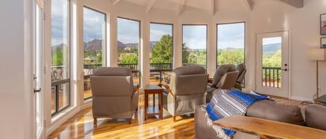 A spacious living room with large windows, a wooden floor, and a view of the mountains.