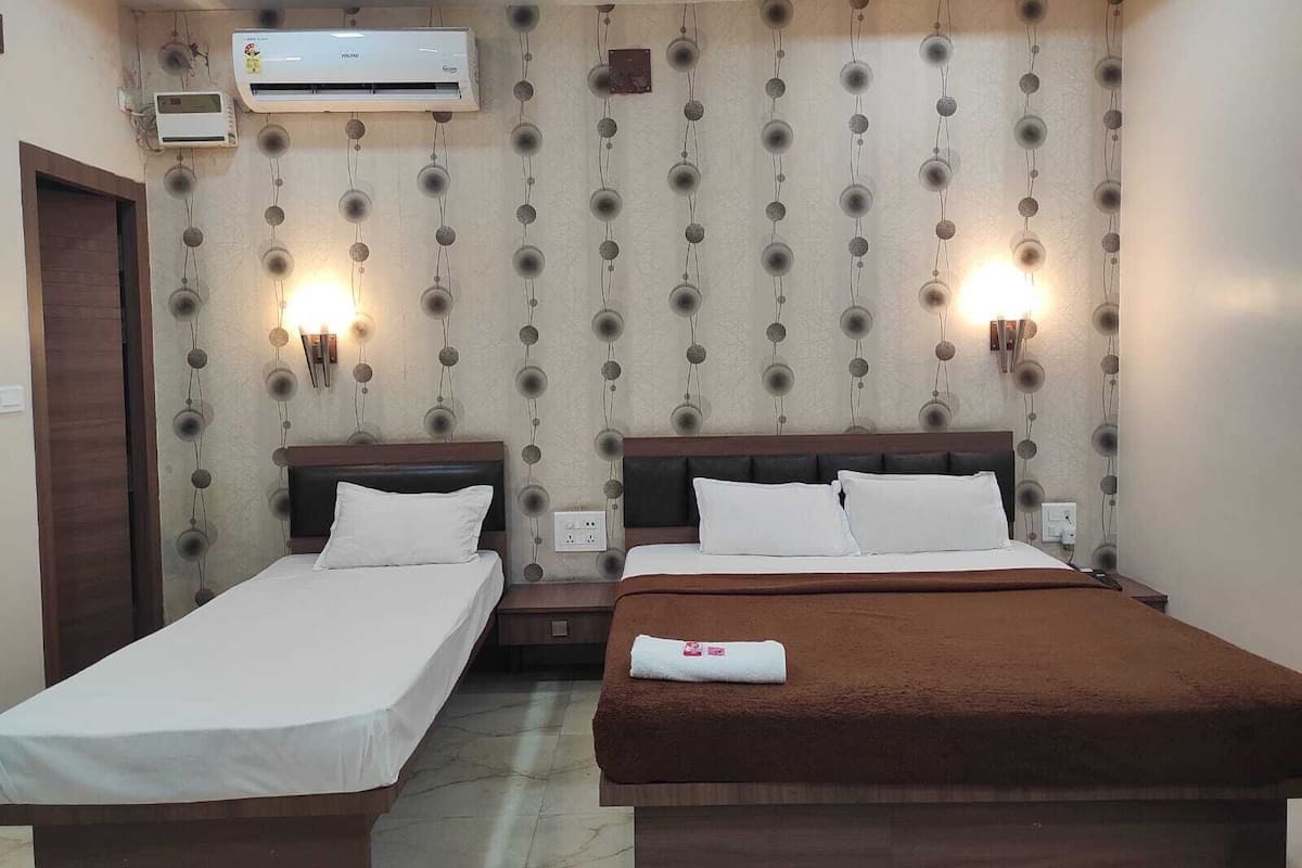 A hotel room with two single beds, a large bed, air conditioning units, and wall-mounted lights.