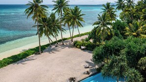Un espace aménagé au bord de la piscine, avec une terrasse en bois, des chaises longues et une vue sur l’océan et les palmiers.