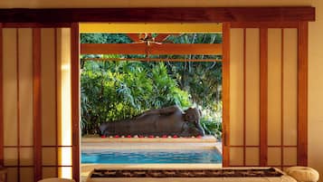 A room with a bed, a view of a pool, and a statue of a reclining figure.