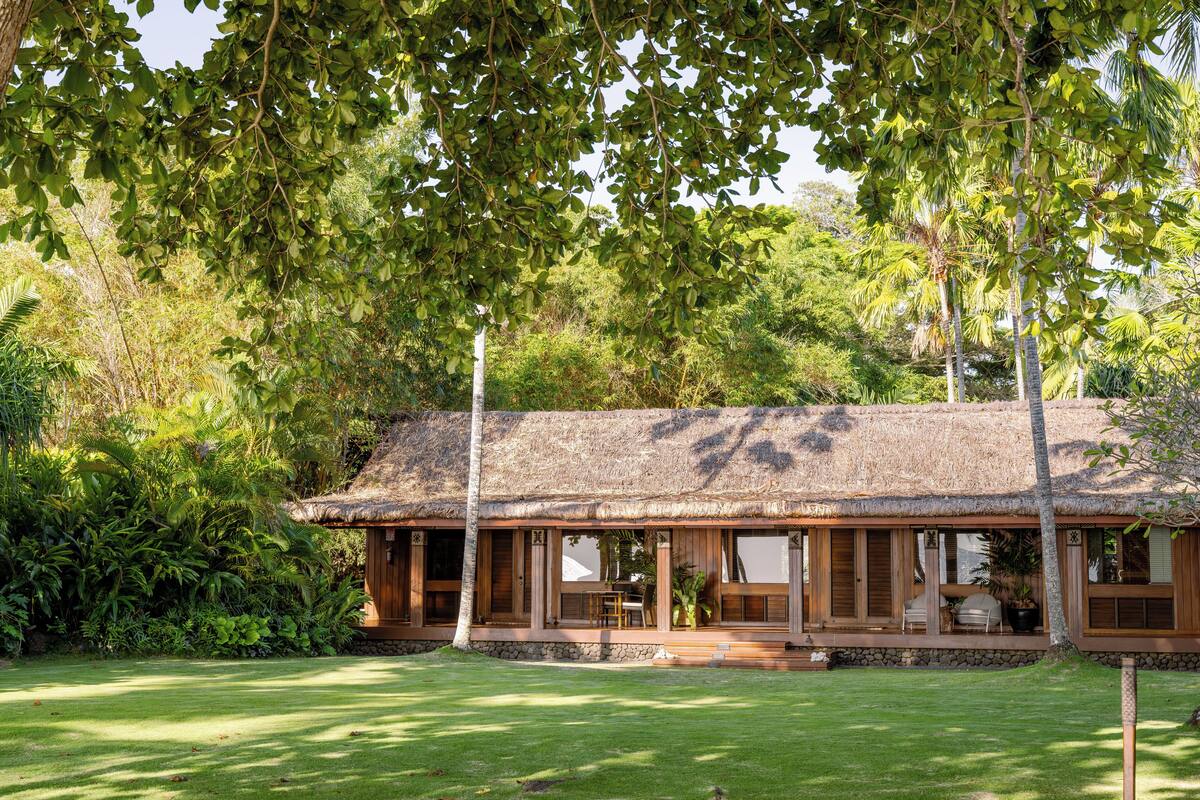 A thatched-roof building with a covered porch, surrounded by lush greenery.