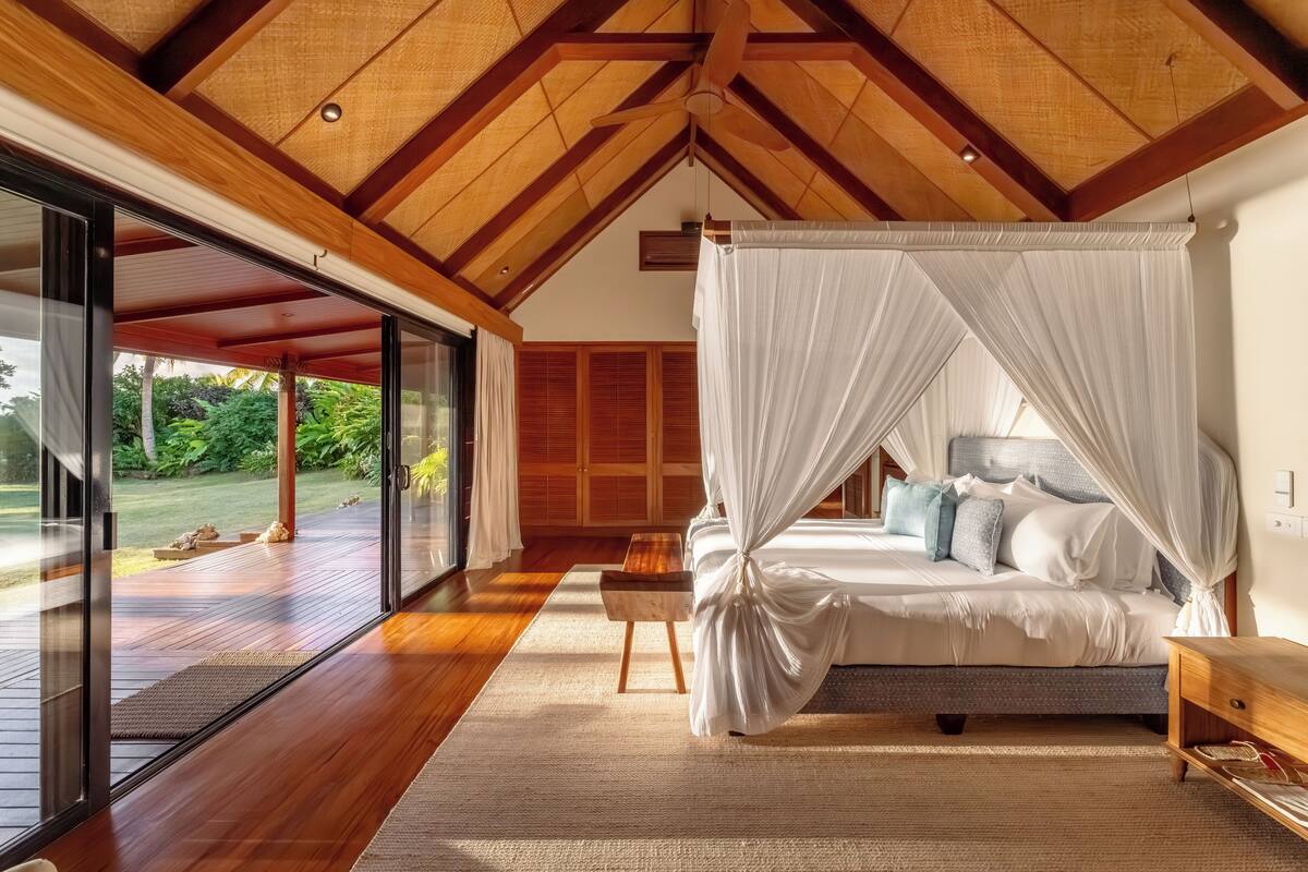 A bedroom with a canopy bed, wooden flooring, and a large sliding glass door leading to an outdoor area.