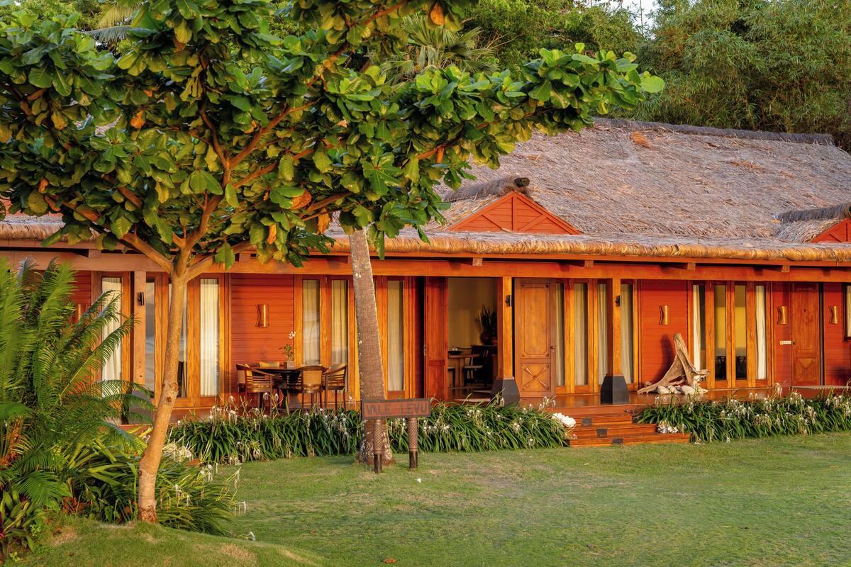 A wooden building with a thatched roof, a covered porch, and a well-maintained lawn.