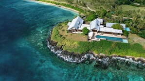 Vue aérienne d’une propriété située sur la côte, avec une piscine, une végétation luxuriante et une plage.