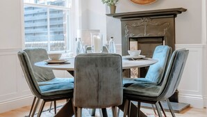 Un coin repas comprenant une table ronde, quatre chaises, une cheminée et une fenêtre avec des stores.