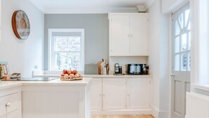 Une cuisine avec des meubles blancs, une grande fenêtre et une porte à panneaux de verre.